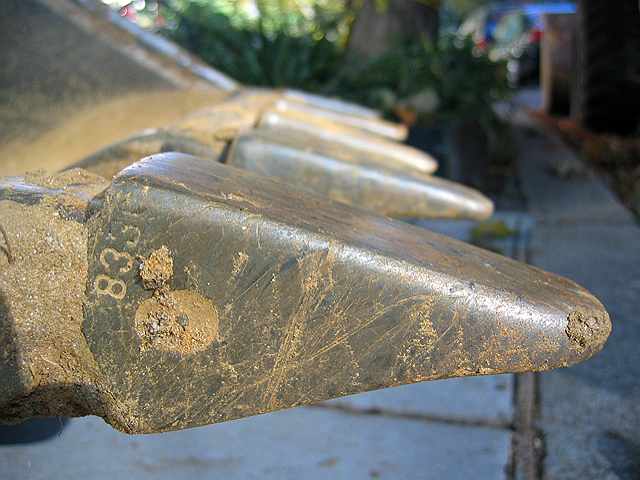 The prongs of a backhoe scoop at rest on our street.