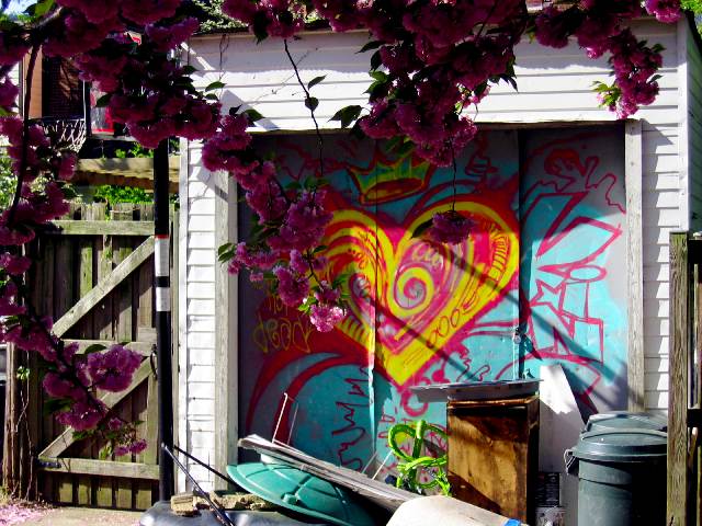 A garage door covered with colorful graffiti and framed by a blooming tree.