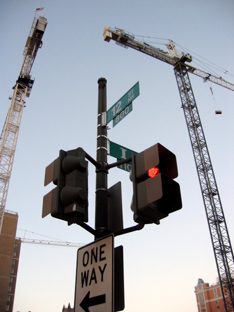 Construction cranes dwarf a light pole near 12th and I St. NW.