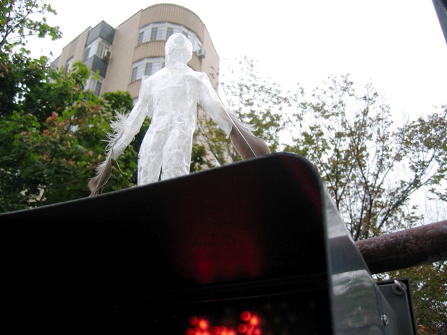 A man made of clear plastic stands atop the crossing light at Mass Ave. and 17th St.